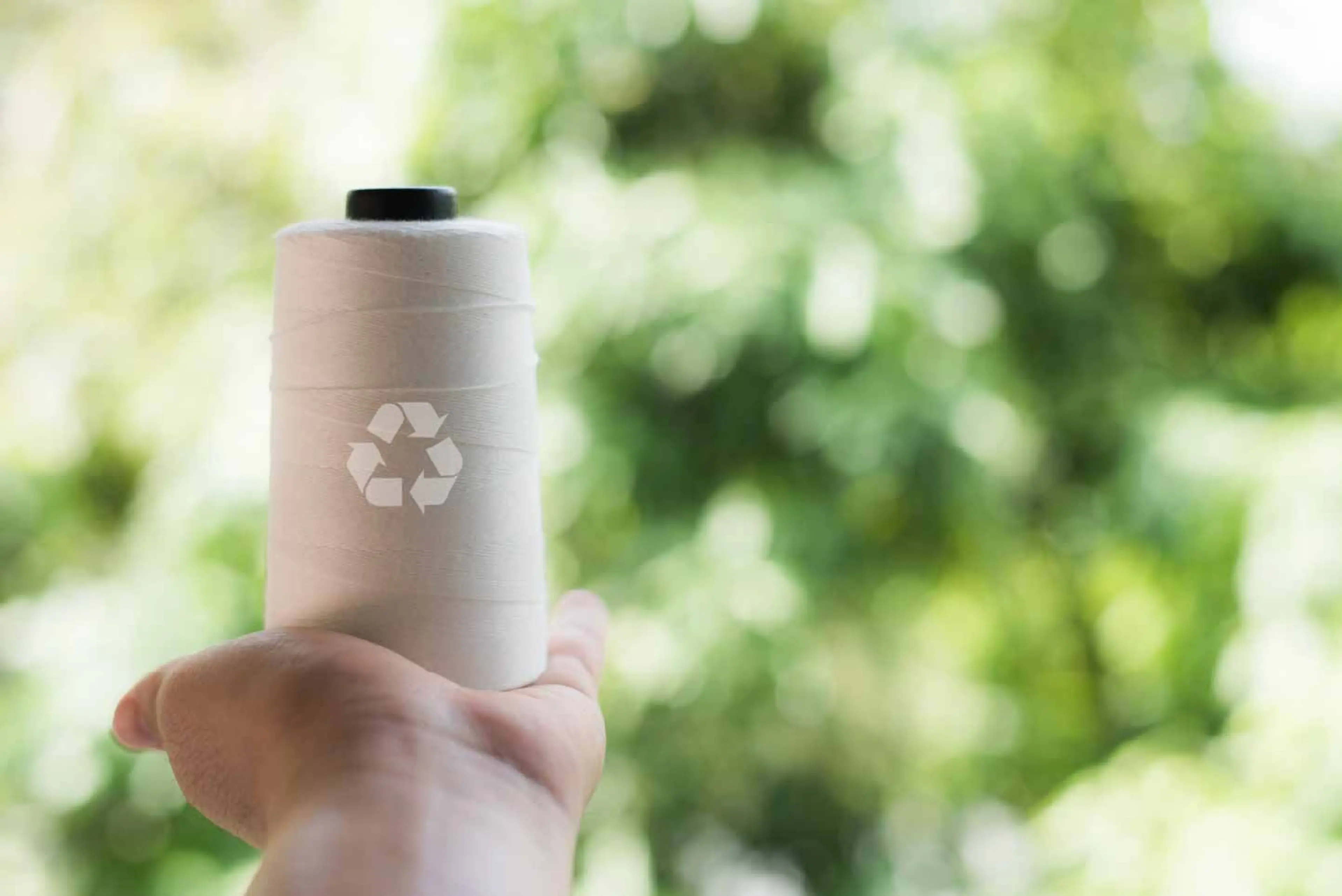 A person displays a spool of white thread with a recycling symbol, highlighting sustainable textile waste management efforts.